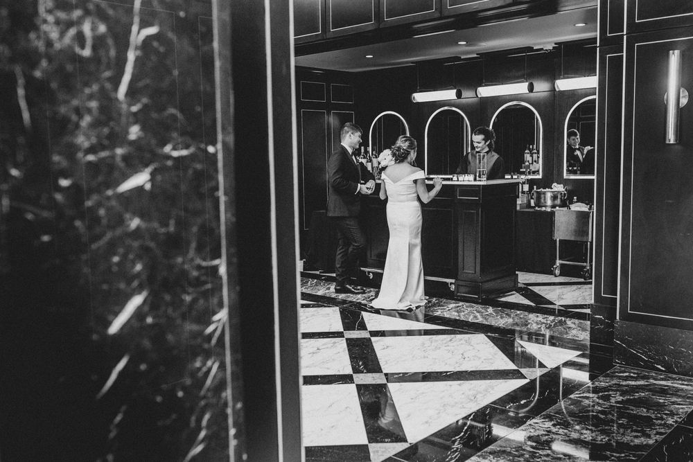 Black and white photo of bride and groom sharing a moment in an elegant hotel lobby with checkered floors.