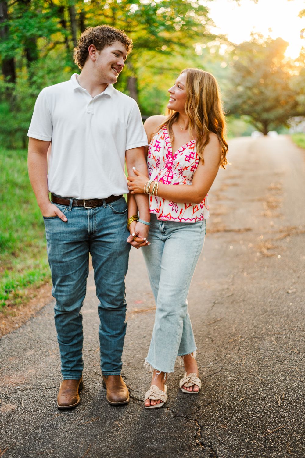 A couple shares a loving glance while walking on a wooded path at sunset.