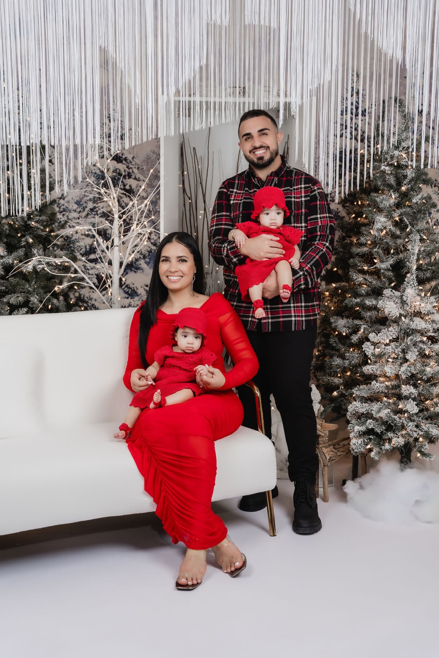 Family holiday portrait with matching red outfits against a winter wonderland backdrop.