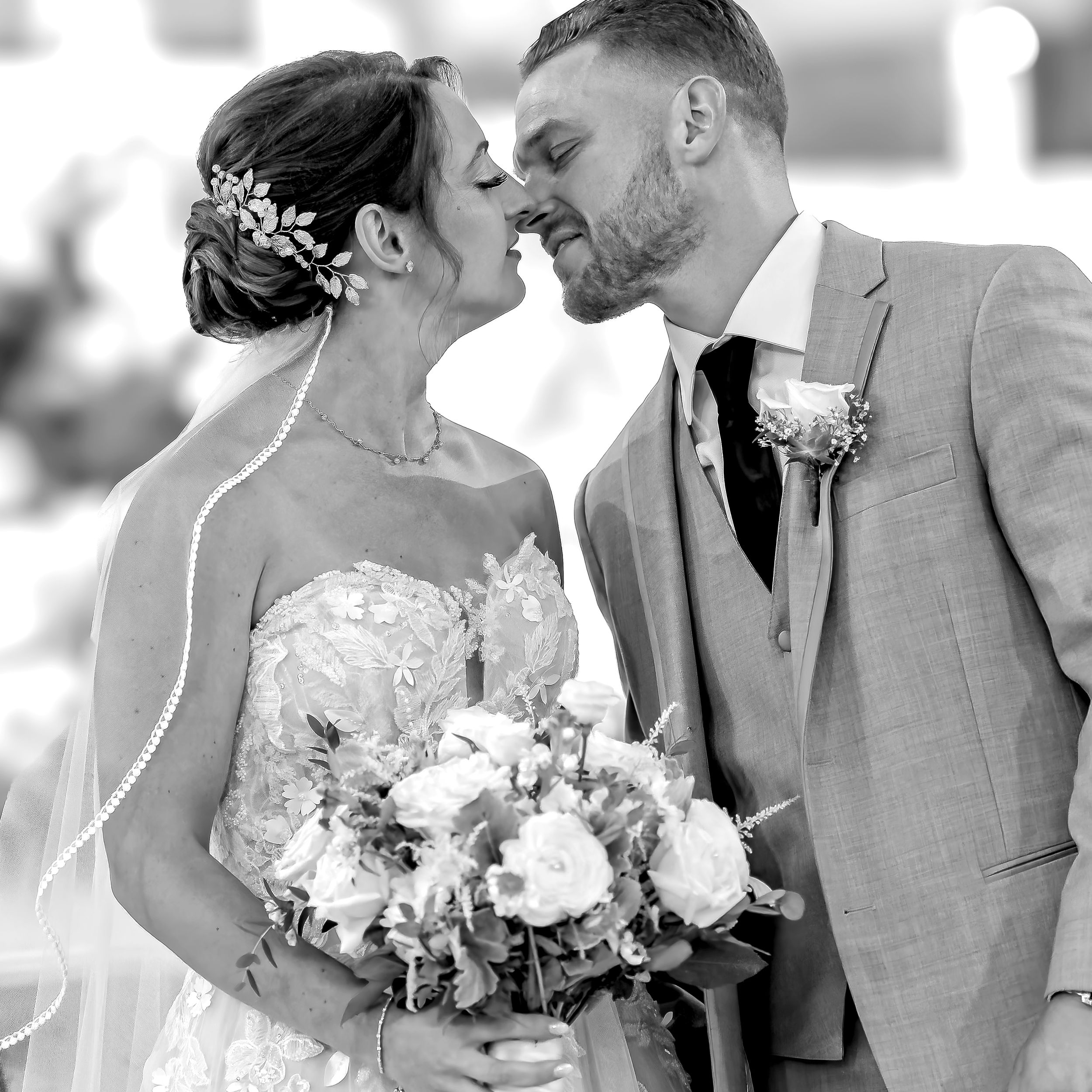 A tender black and white wedding moment with bride holding white bouquet as couple shares intimate kiss.