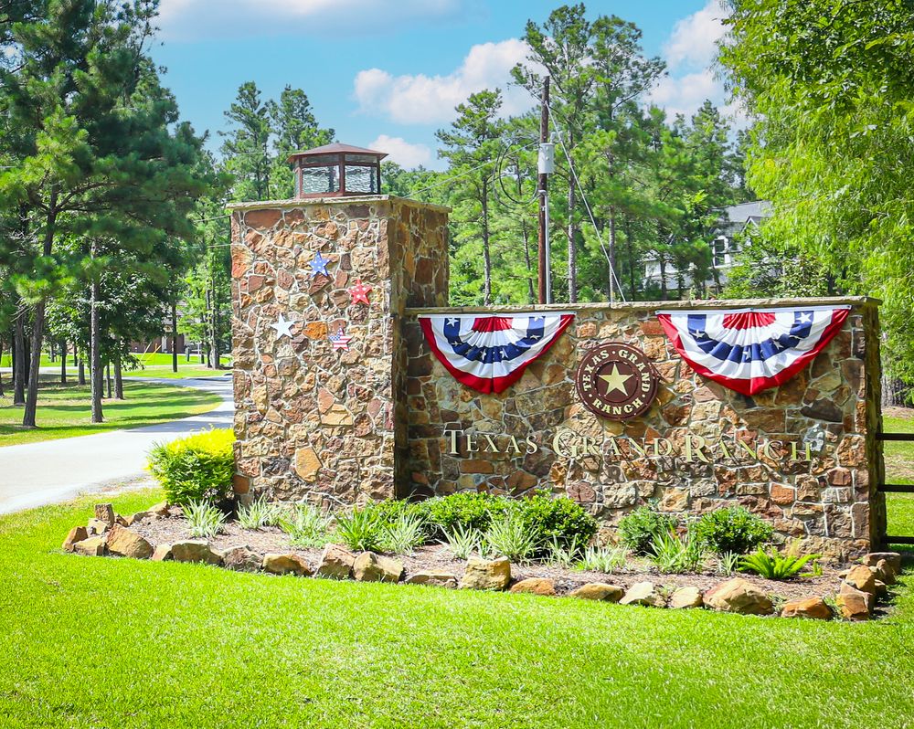 Texas Champions Club entrance sign adorned with patriotic bunting, surrounded by lush green trees and manicured lawn.