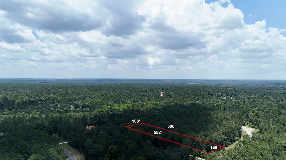 Aerial drone view of a densely wooded land parcel with red measurement lines showing property dimensions of 168, 585, 582, and 140 feet.