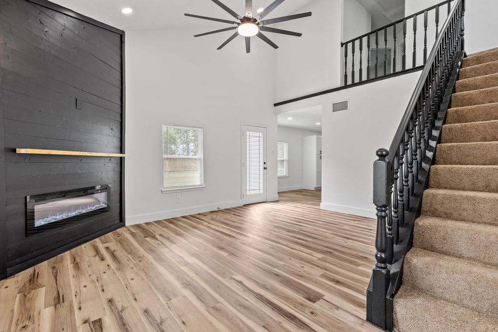 Bright foyer with hardwood floors, black staircase, high ceilings, ceiling fan, and modern fireplace.