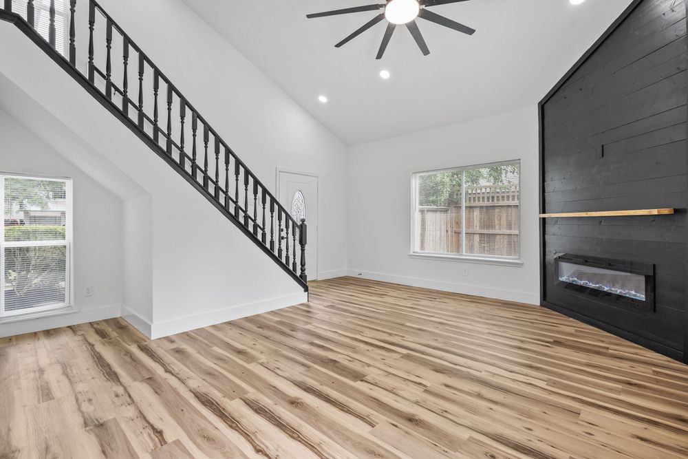 Bright open living room with hardwood floors, vaulted ceiling, ceiling fan, black staircase, and modern fireplace.
