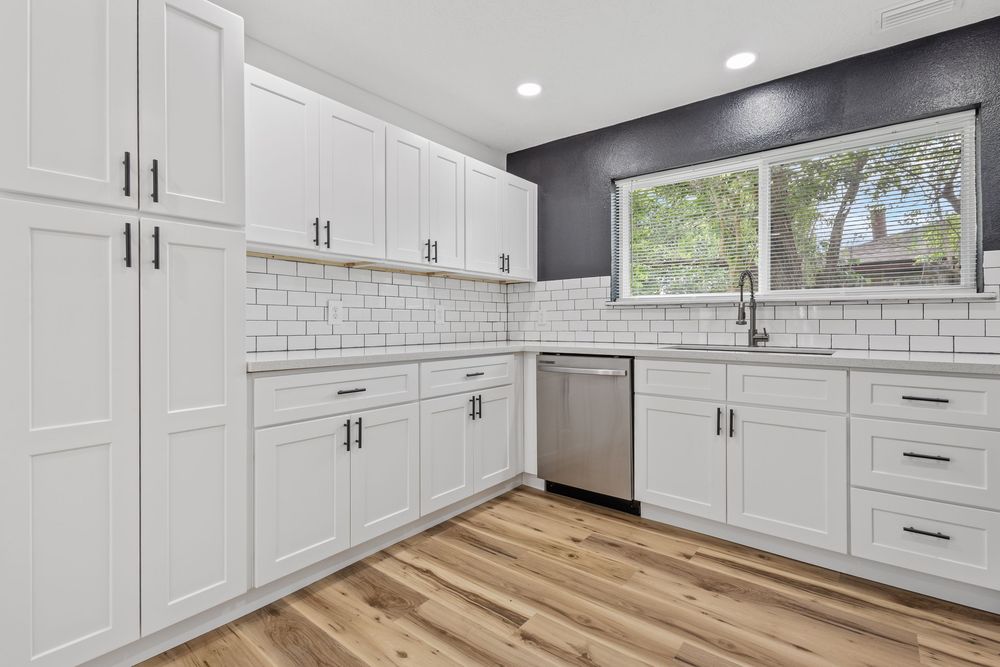 Modern white shaker kitchen cabinets with subway tile backsplash, stainless steel dishwasher, and light hardwood floors.