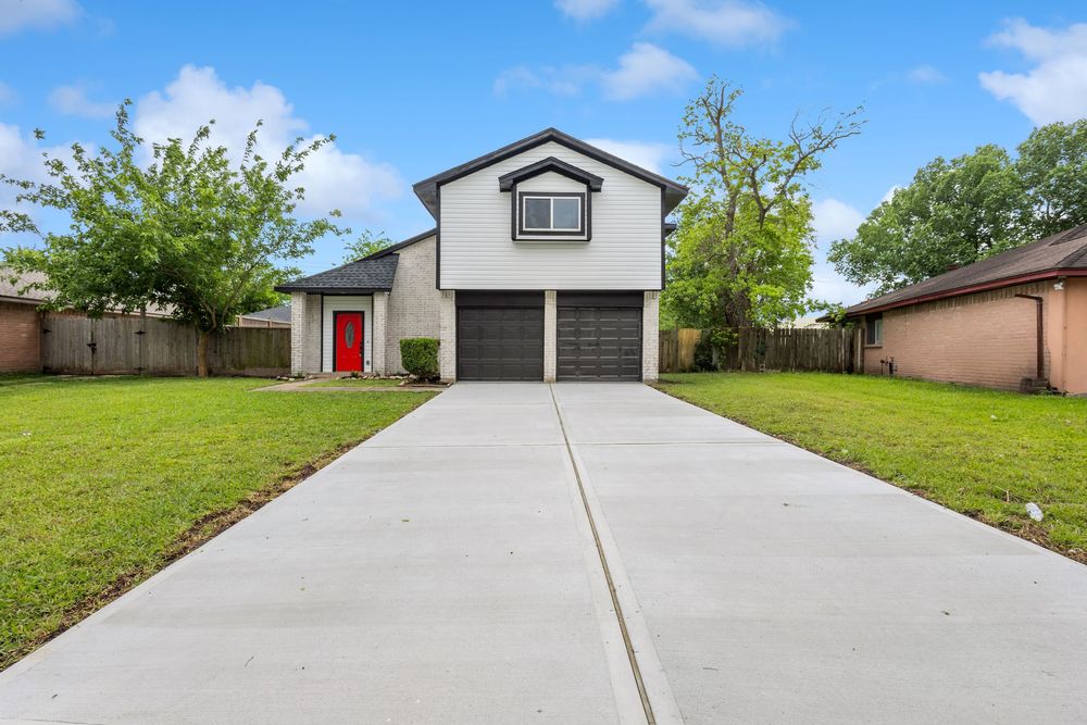 Two-story home with gray exterior, red front door, two-car garage, concrete driveway, and lush green lawn.