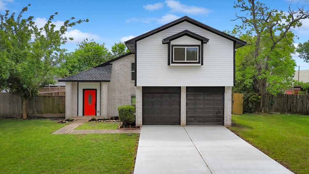 Two-story home with white siding, red front door, double dark garage doors, concrete driveway, and lush green lawn.