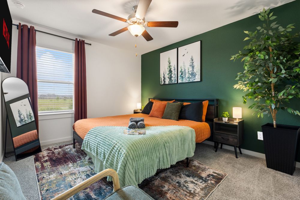 Cozy bedroom with green accent wall, orange bedding, ceiling fan, and decorative plant in a modern home.