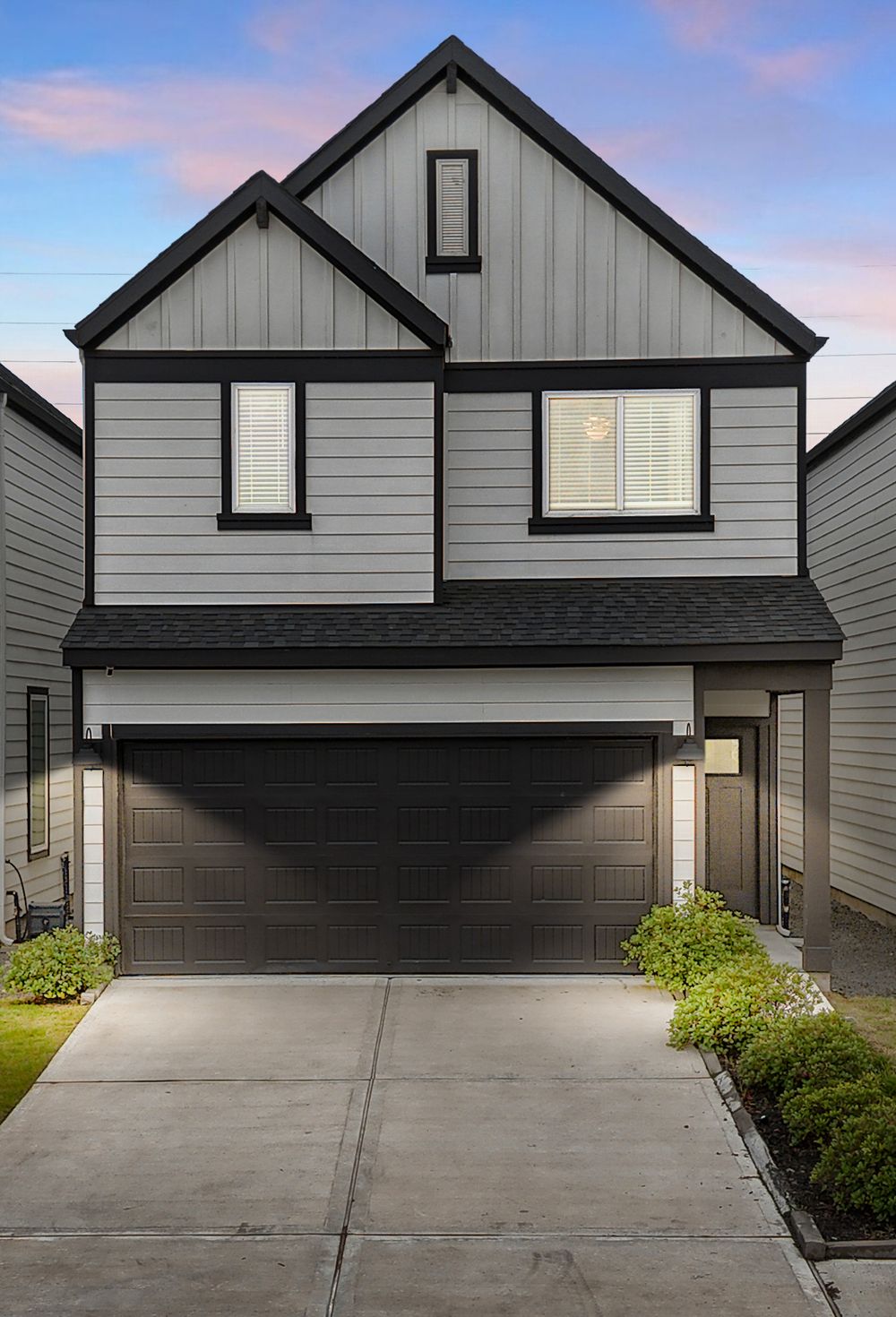 Modern two-story gray and black farmhouse-style home with dark garage door and concrete driveway at dusk.