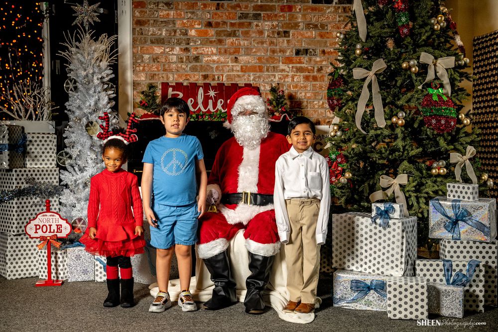 Santa Claus poses with children next to decorated Christmas trees and wrapped presents.