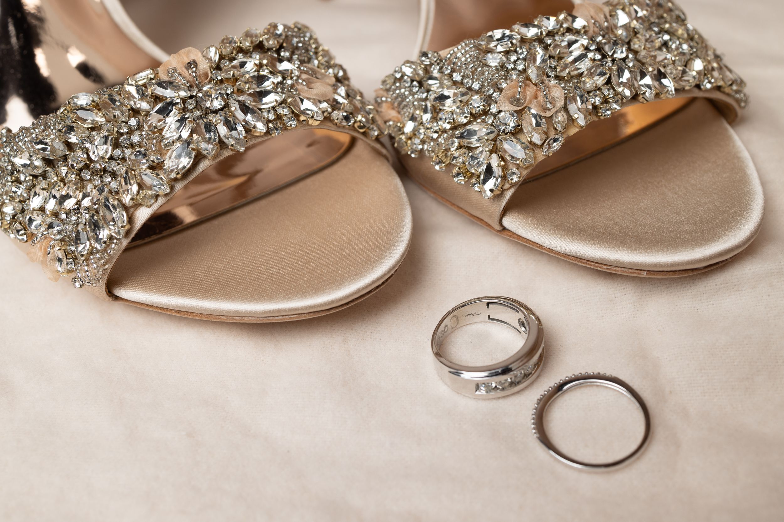 Sparkly bridal sandals with crystal embellishments next to wedding rings on light fabric.