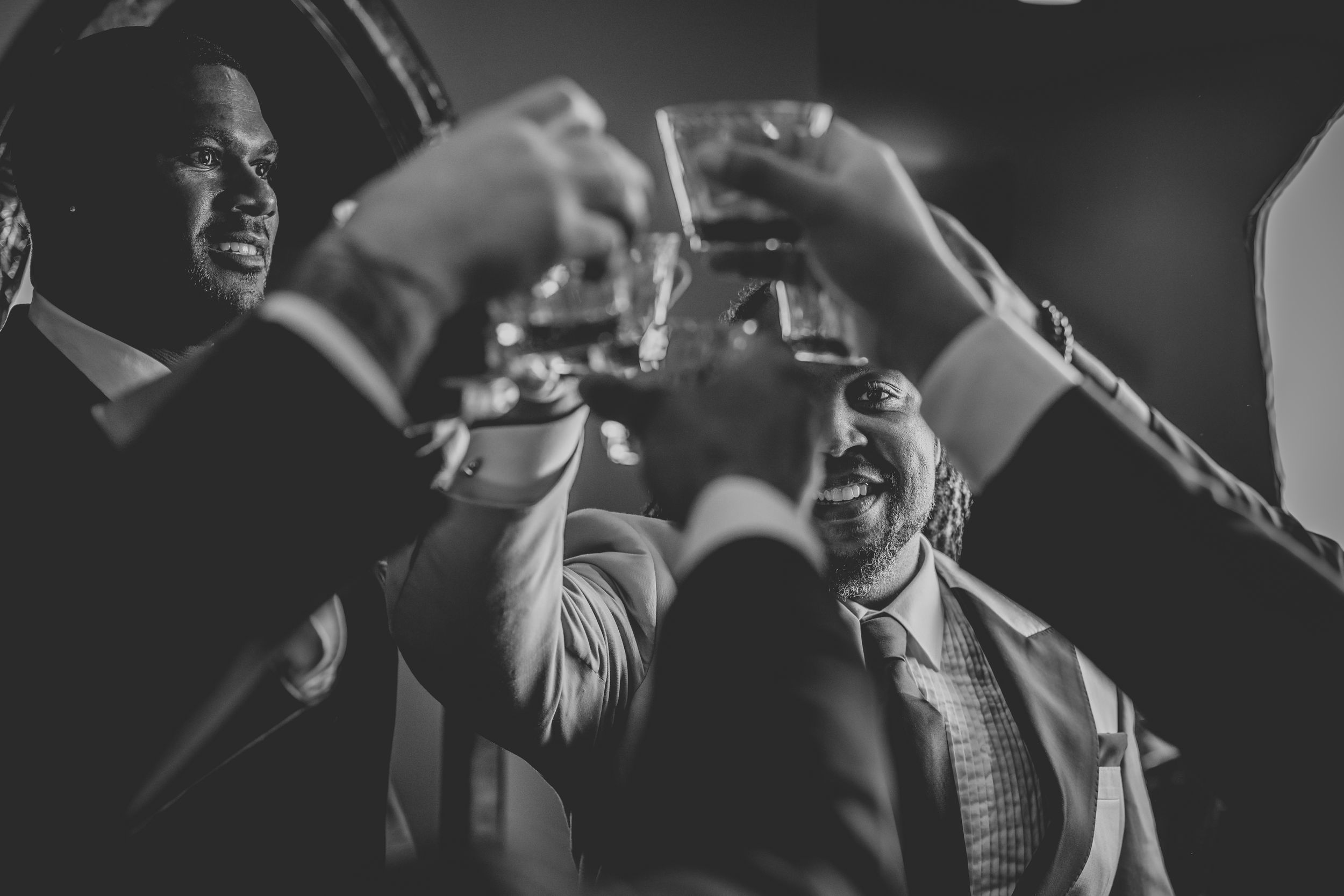 A joyous celebration moment captured in black and white as guests raise their glasses in a toast at an indoor event.