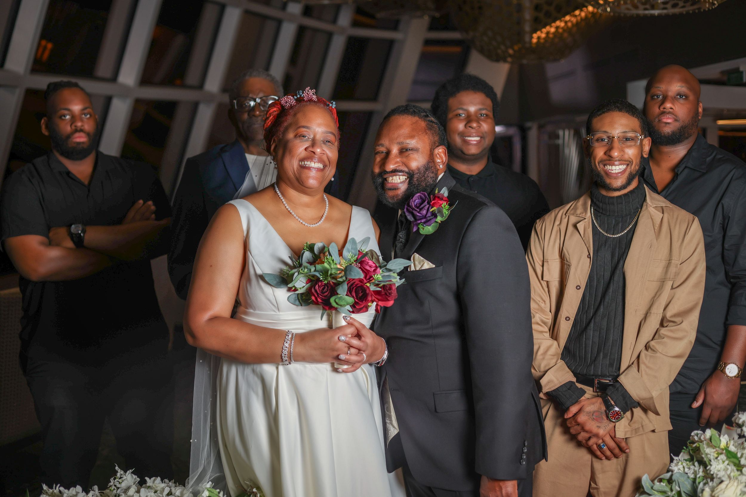 Wedding party poses together with bride holding colorful bouquet at indoor celebration venue.