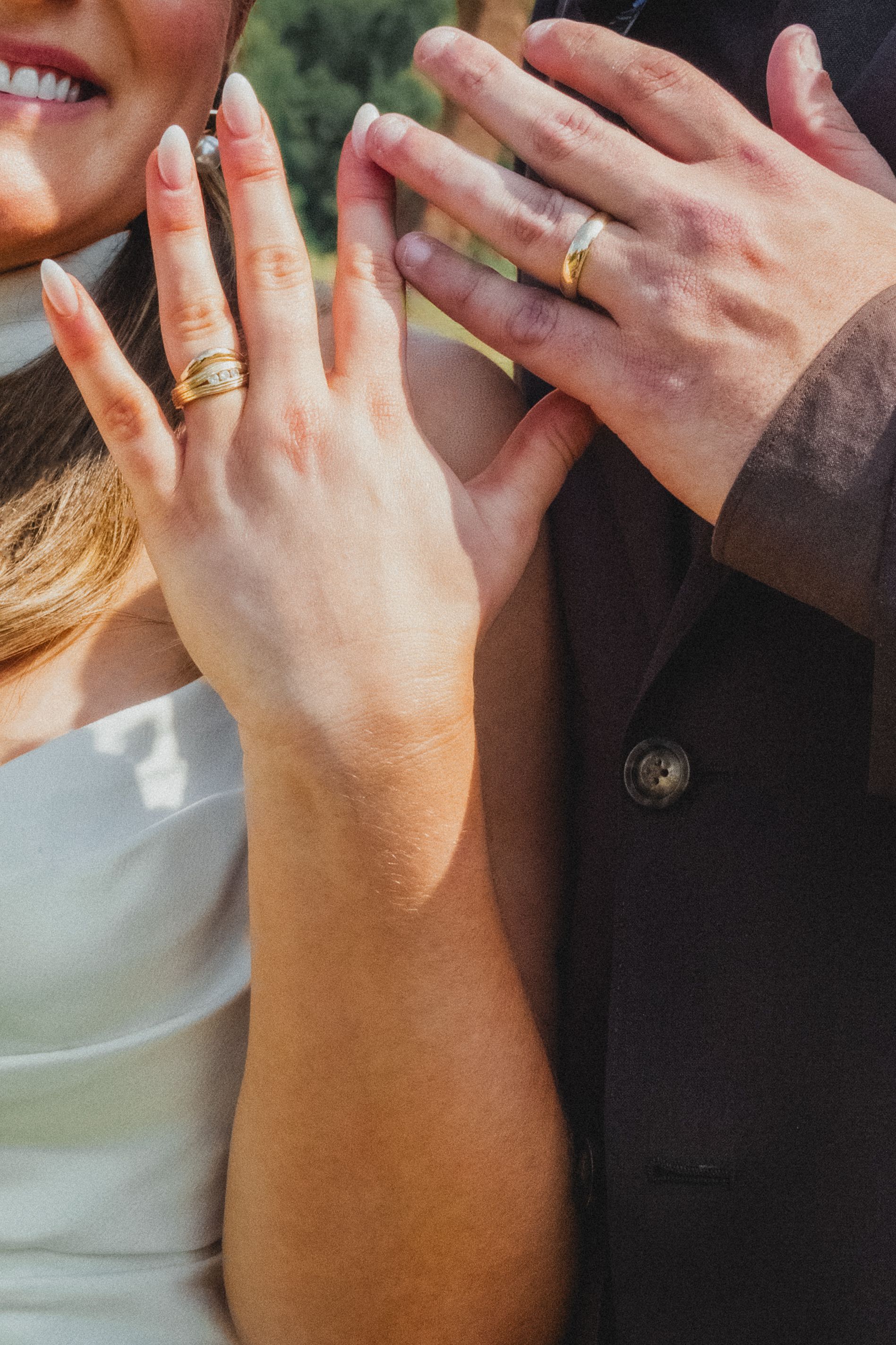 Bride and groom showing off wedding rings, woman wearing gold diamond band, man in black suit, close-up detail shot.