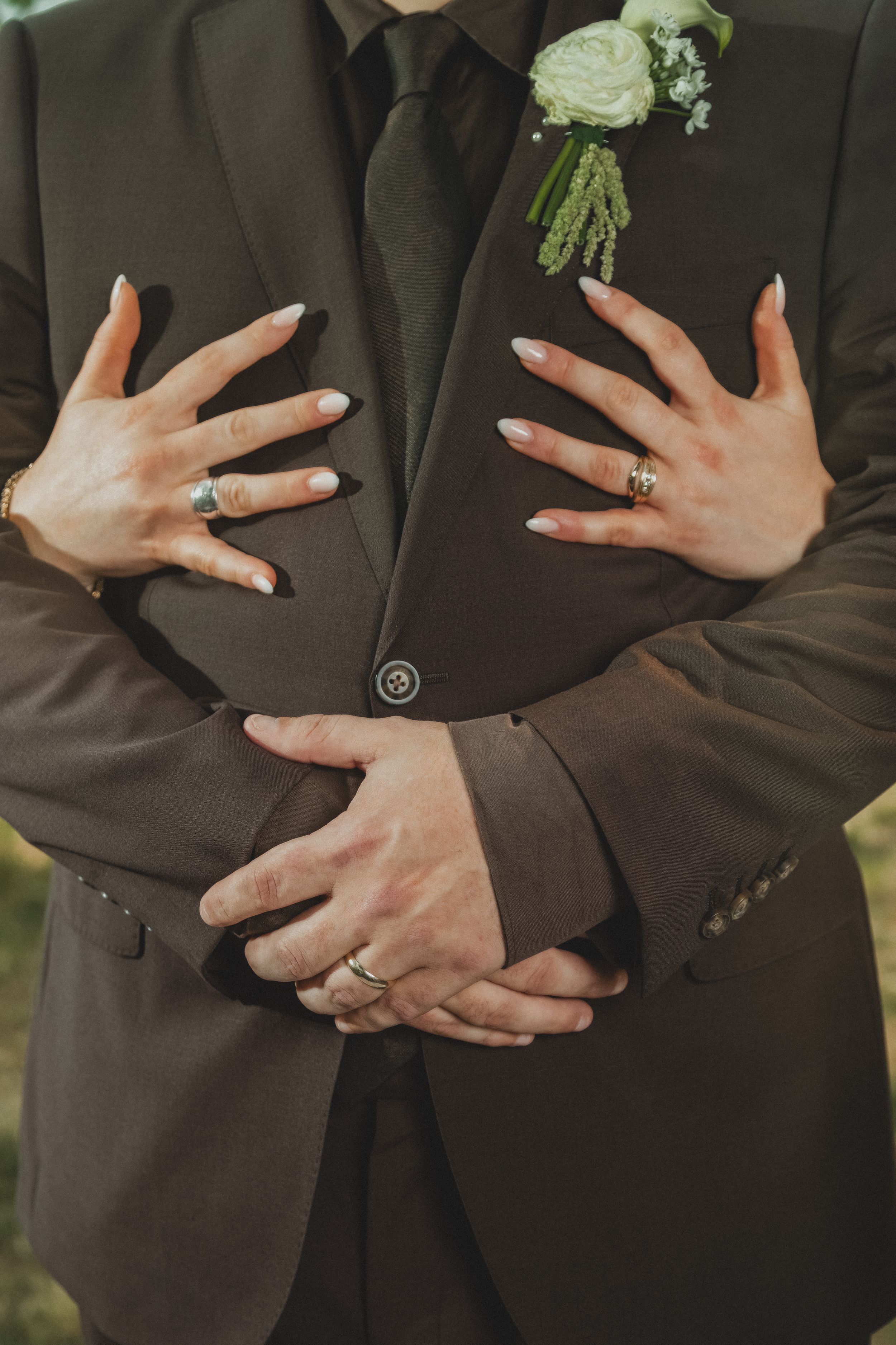 Bride's hands with rings embracing groom in dark suit with white boutonniere at wedding ceremony.
