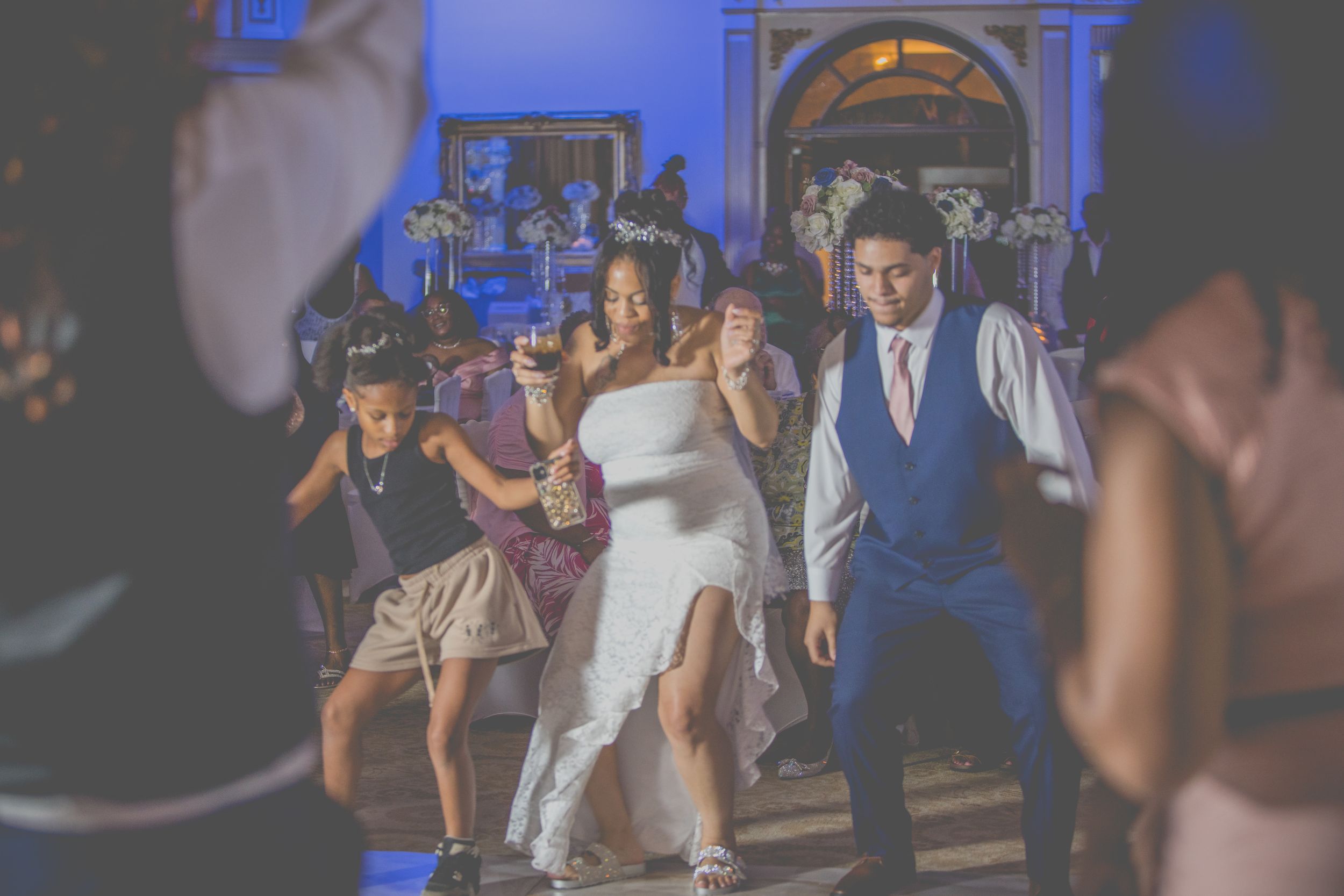 Wedding guests dance and celebrate on a blue-lit dance floor at an evening reception.