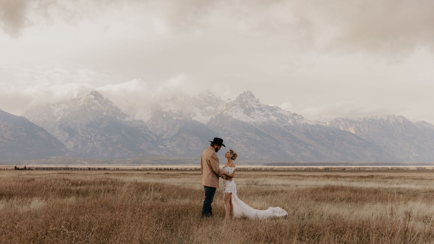 Panoramic view of a couple on a mountain ridge against a dramatic mountainous landscape.