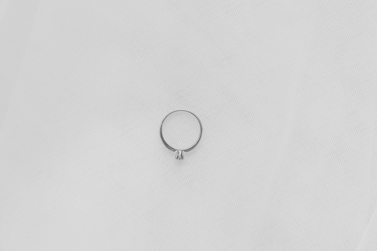 A minimalist photograph of a single silver ring on a light gray background.