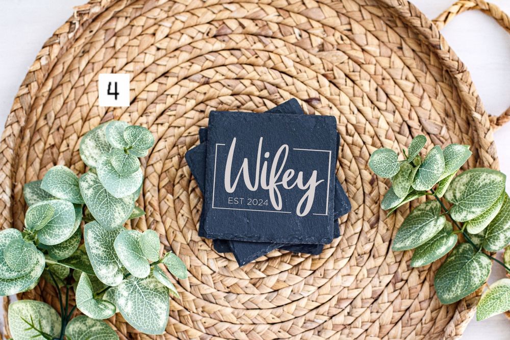 Navy blue wedding coaster with 'Wifey' text displayed on woven charger with greenery accents.