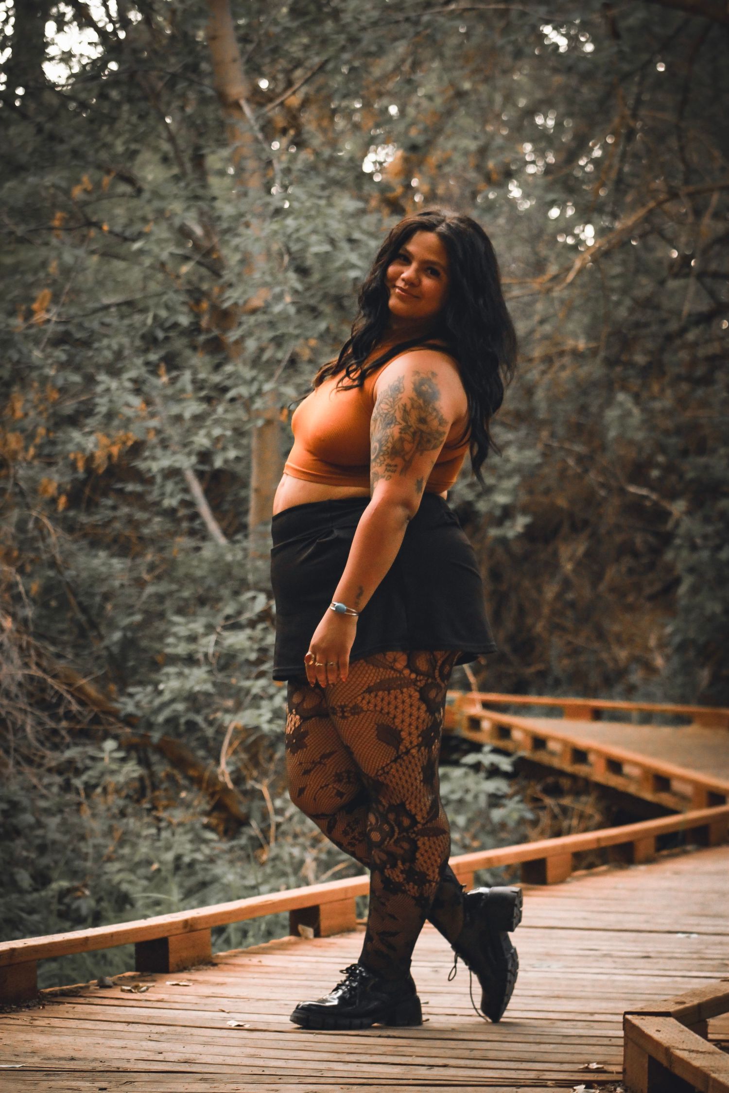 Someone poses on a wooden boardwalk in casual attire with tattoos visible.