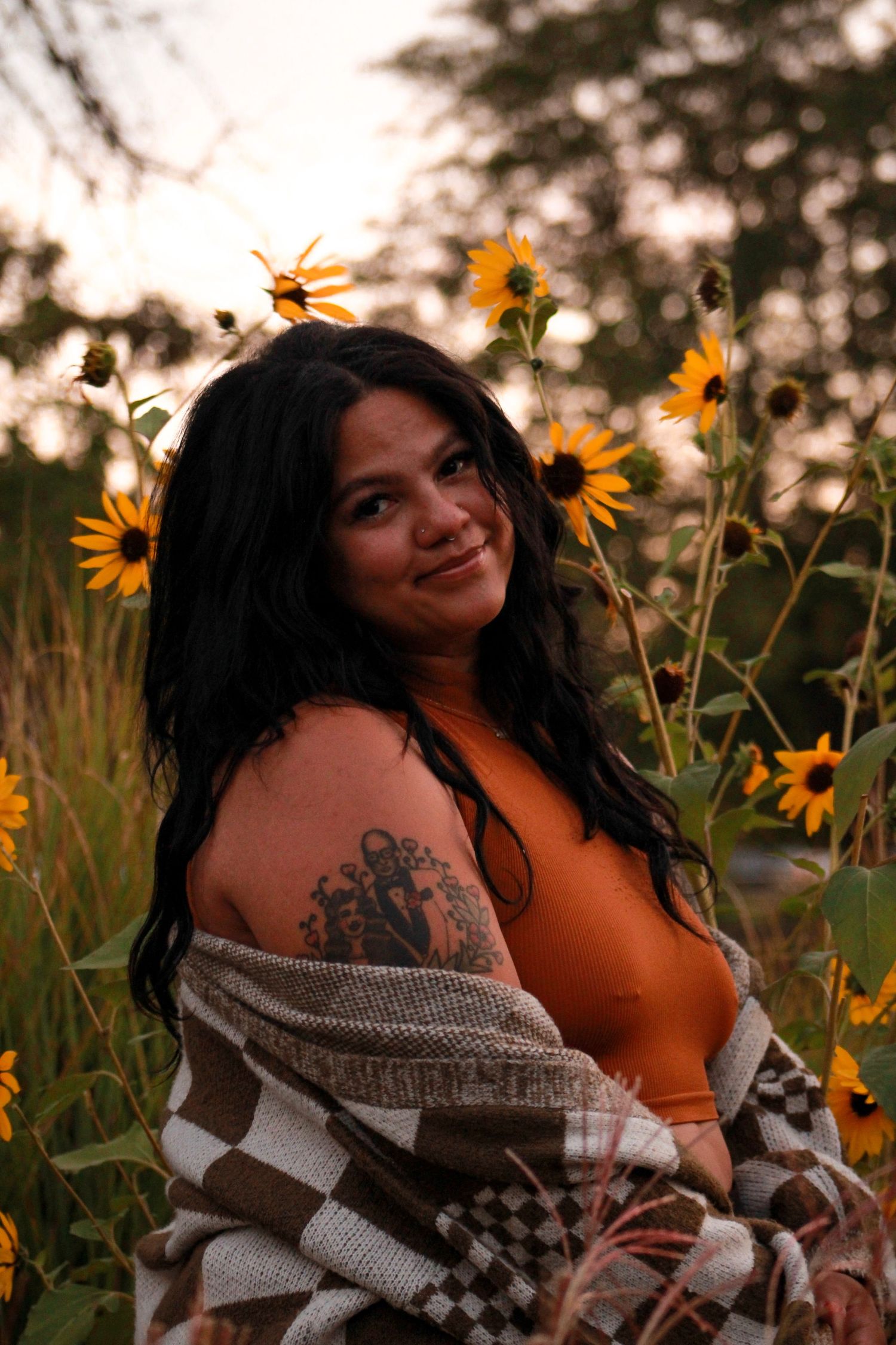 A sunset portrait among blooming sunflowers wearing a striped cardigan and orange top.