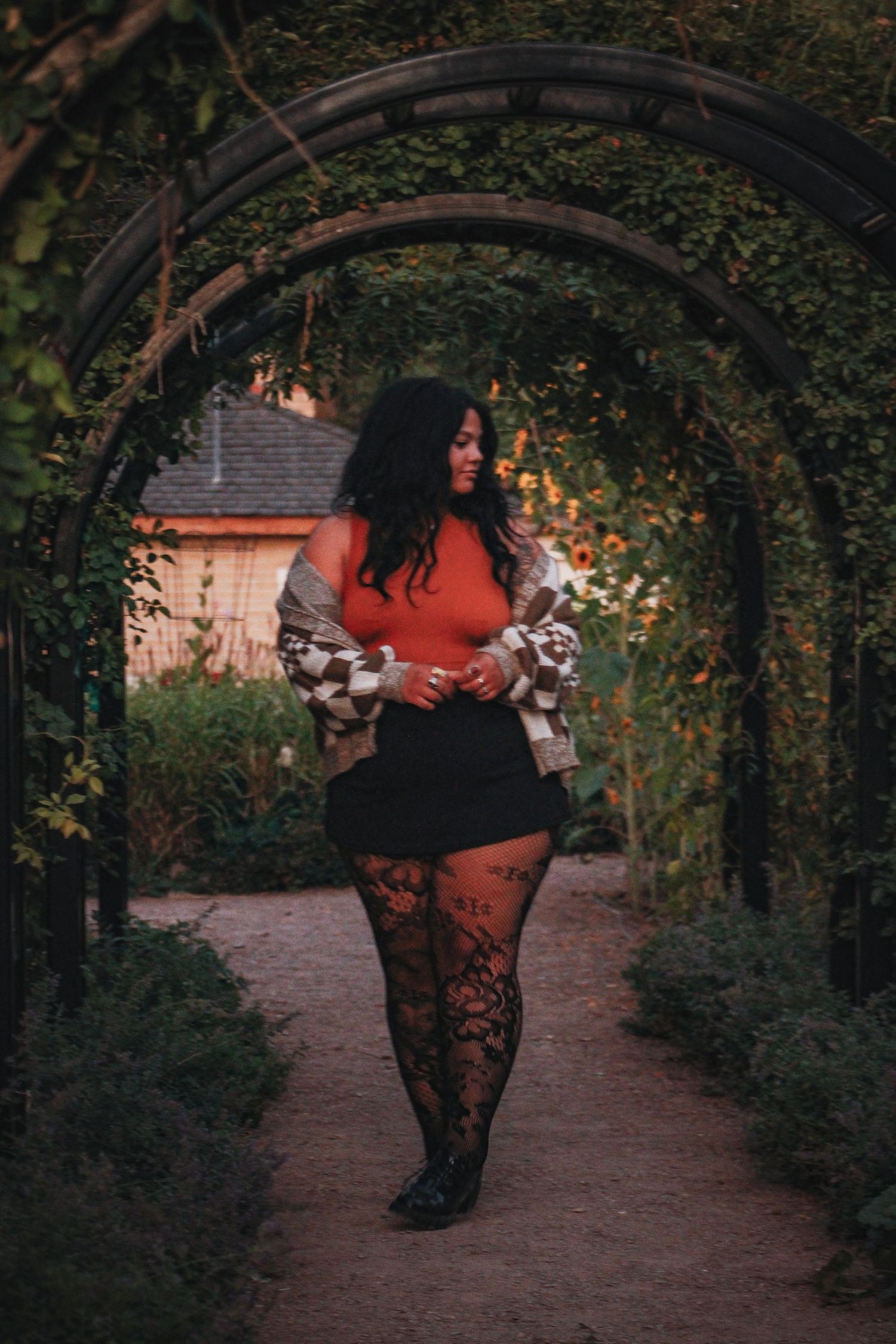 A stylish pose under a garden archway wearing lace tights and a checkered sweater.