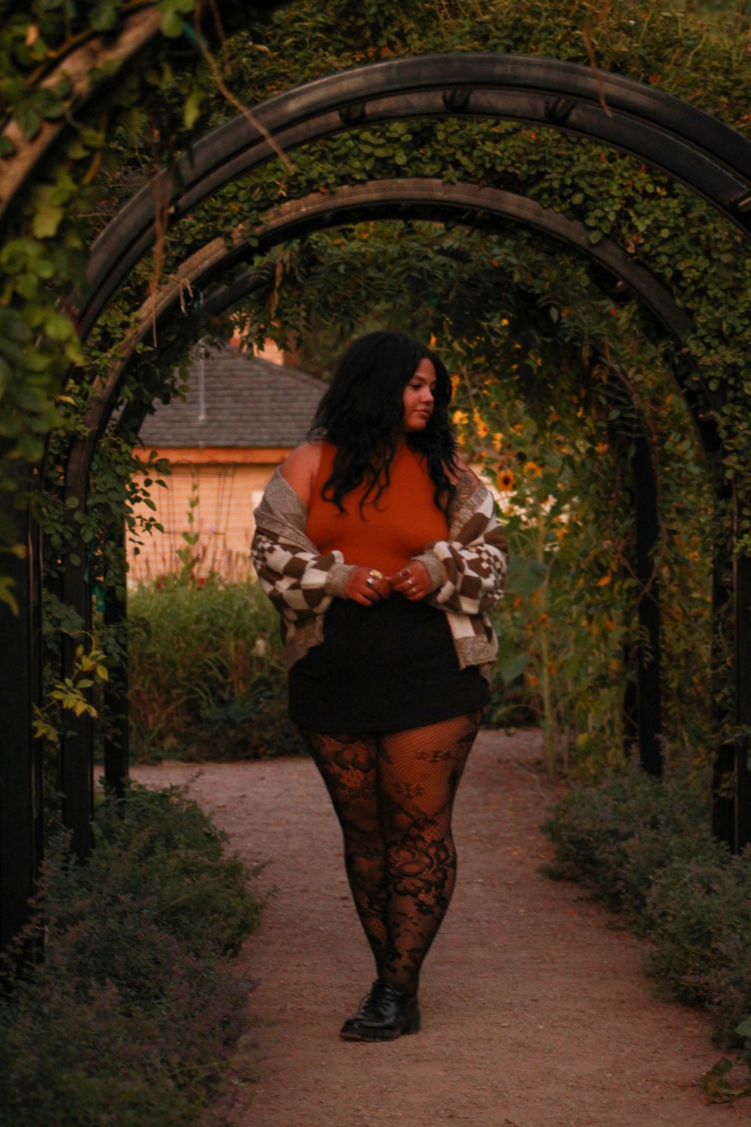 A fashion portrait under a vine-covered garden arch at sunset.