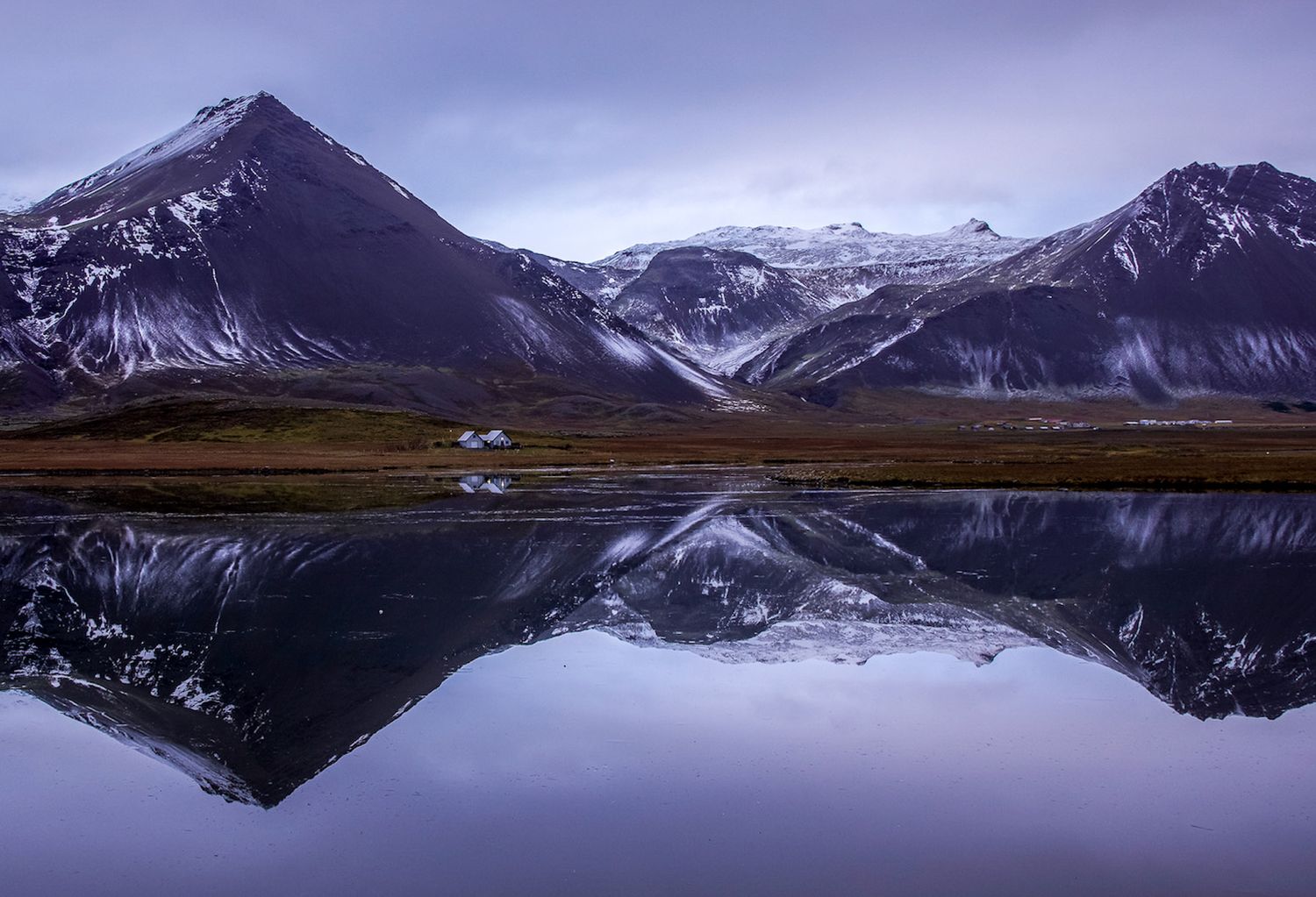 Tidal pool reflecting mountains and a small white house in iceland