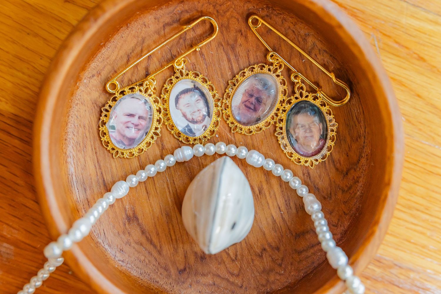 Vintage cameo brooch pins and pearl necklace displayed on a wooden plate.