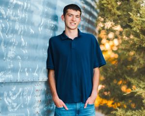 A person in a navy blue shirt and jeans poses outdoors against a blurred nature background with golden sunlight.