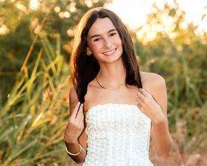 A person in a white lace dress poses outdoors during golden hour with sunlit grass in the background.