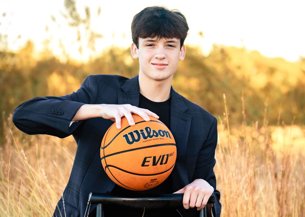 Young man in suit holding Wilson EVO basketball outdoors in golden field during sunset photography session.