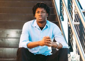 Person in light blue shirt sitting on stairs while looking at smartphone in urban setting.