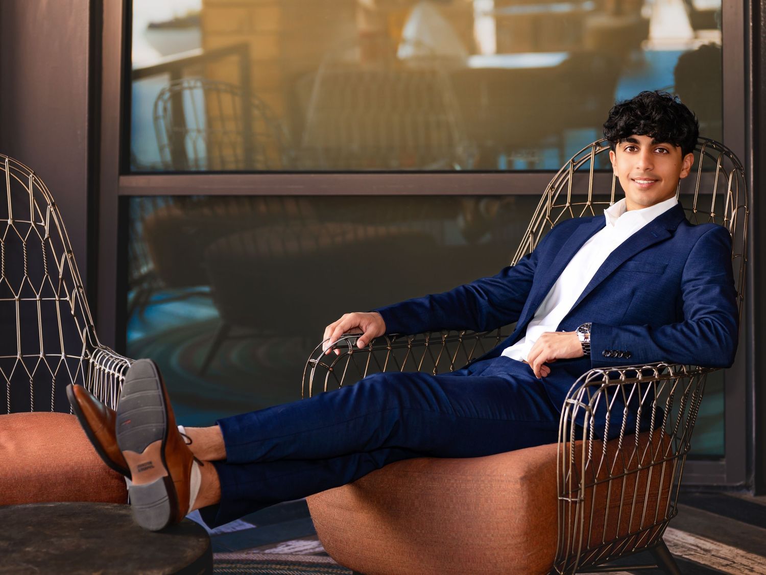 A person in a navy blue suit lounges on a metal bench in an industrial-style setting.