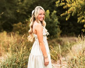 Woman in white dress smiling and twirling in golden sunlit field during sunset photoshoot.