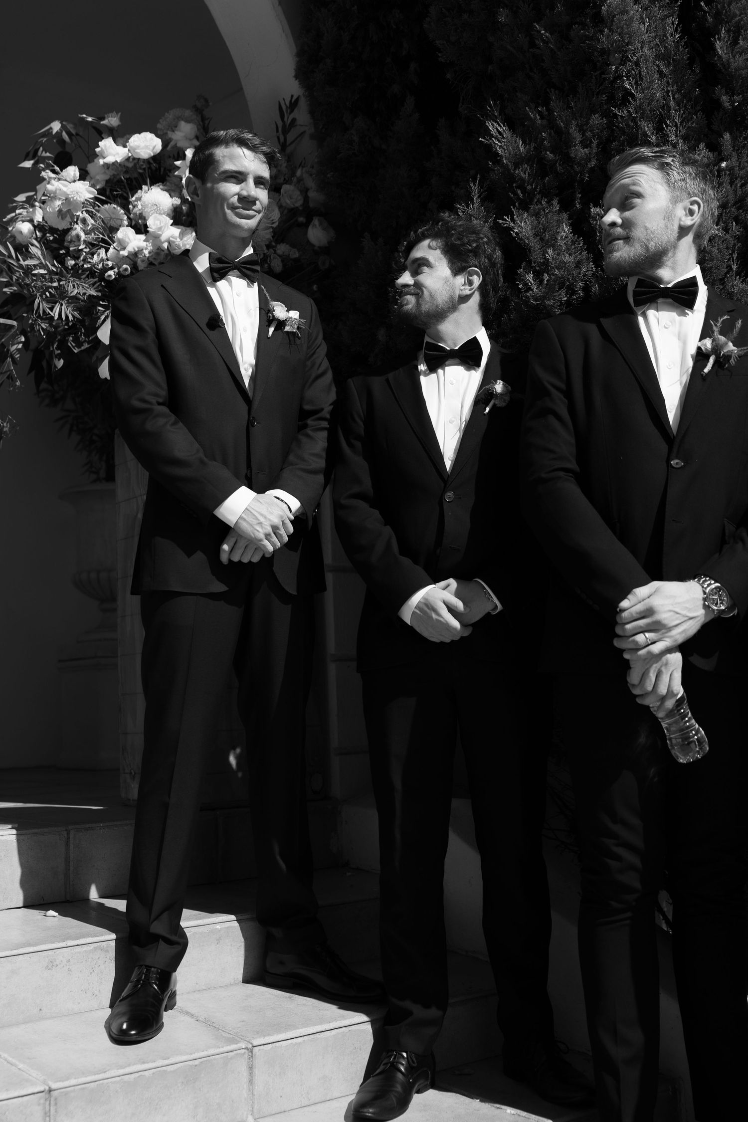 A series of black and white photos showing groomsmen in formal suits standing together at a wedding ceremony.