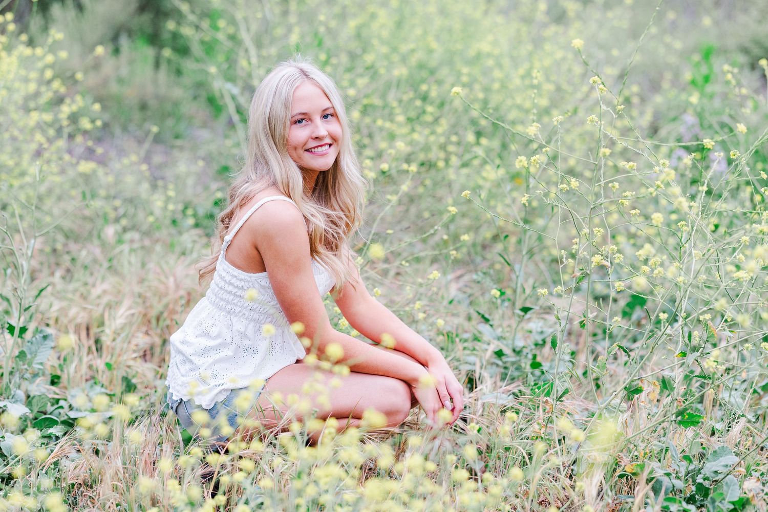 A person in a white summer dress poses against a birch tree trunk in a natural outdoor setting.