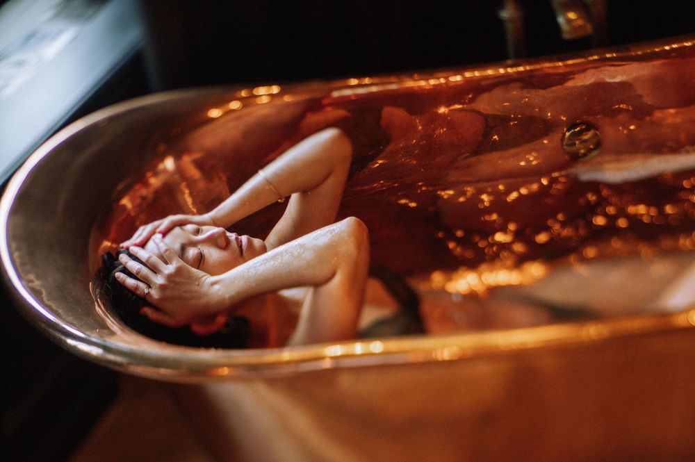 Artistic composition of body parts reflected in copper-toned liquid surface.