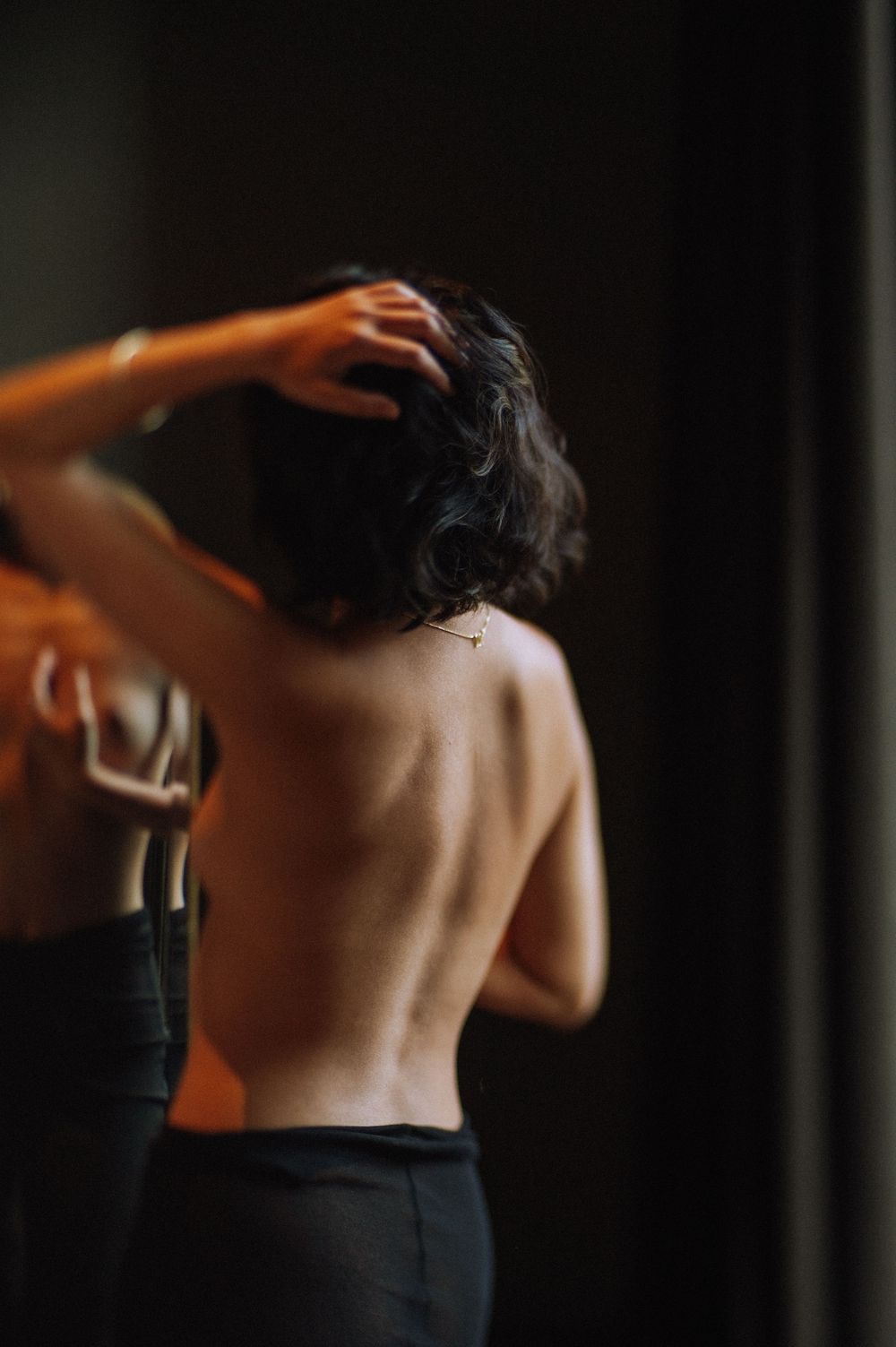Reflective moody portrait of woman with short hair seen through a mirror in warm, intimate setting.