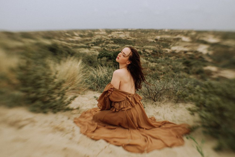 Woman in flowing dress sitting on sand dunes outside Amsterdam, surrounded by natural landscape.