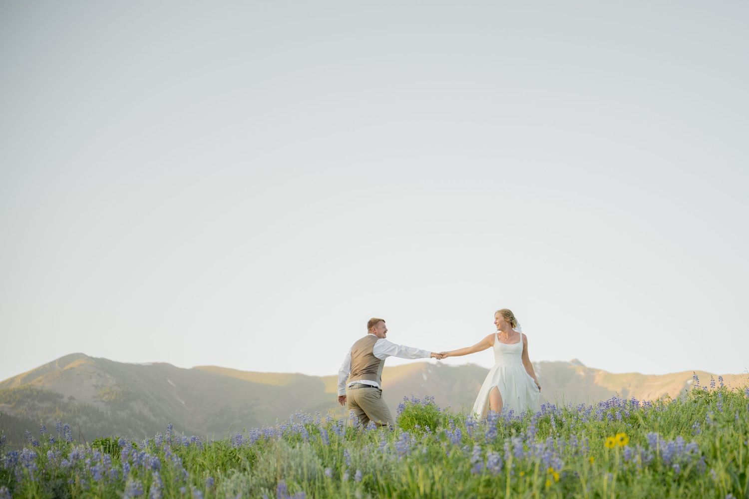 Couple sits on a hillside blanket overlooking a scenic mountain valley at sunset.