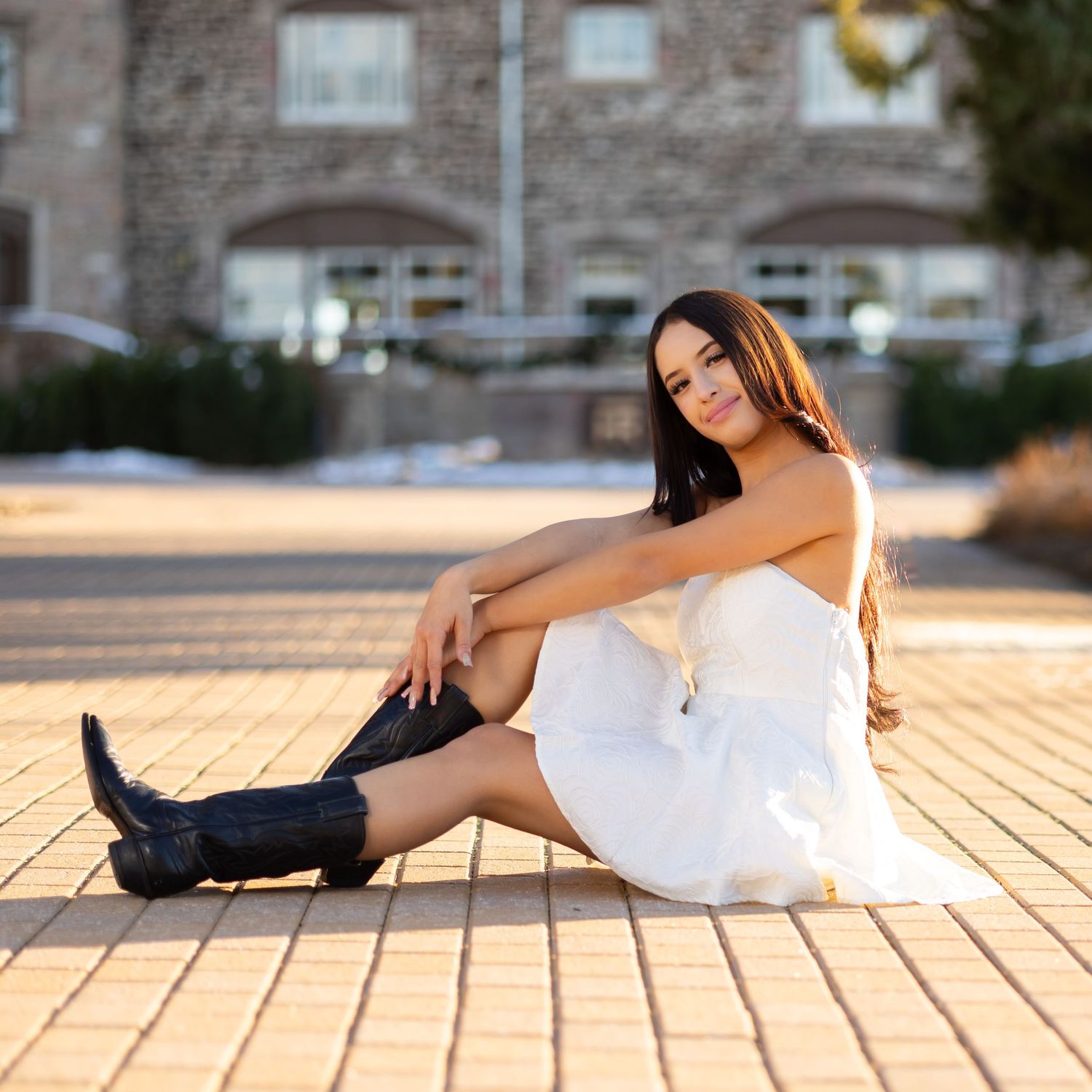 A white sundress outfit paired with black boots creates a stylish look on brick pavers at sunset.