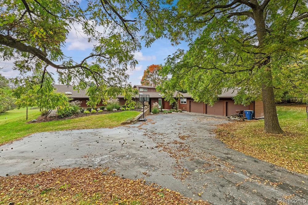 Ranch home exterior with large driveway, mature trees, and attached garage.