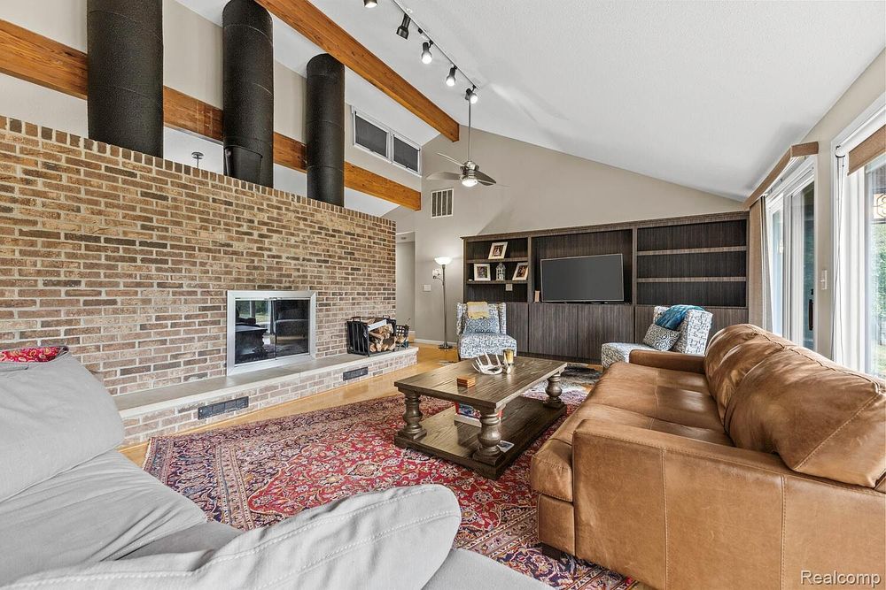 Vaulted ceiling living room with brick fireplace, leather sofa, and built-in shelving.