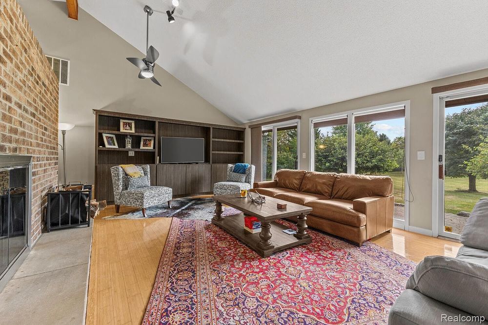 Bright living room with vaulted ceiling, ceiling fan, large windows, and hardwood floors.