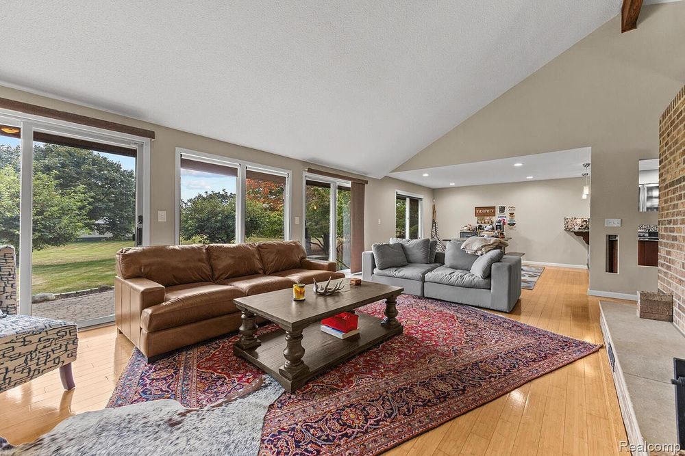 Sunlit living room with vaulted ceiling, large windows, hardwood floors, and open floor plan.