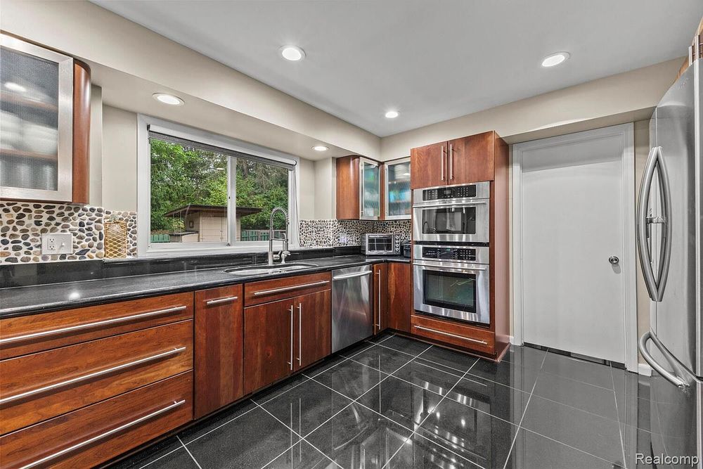 Modern kitchen with cherry cabinets, dark granite counters, stainless appliances, and tile floors.