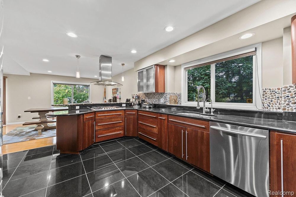 Modern kitchen with cherry wood cabinets, stainless steel appliances, dark granite countertops, and black tile floors.