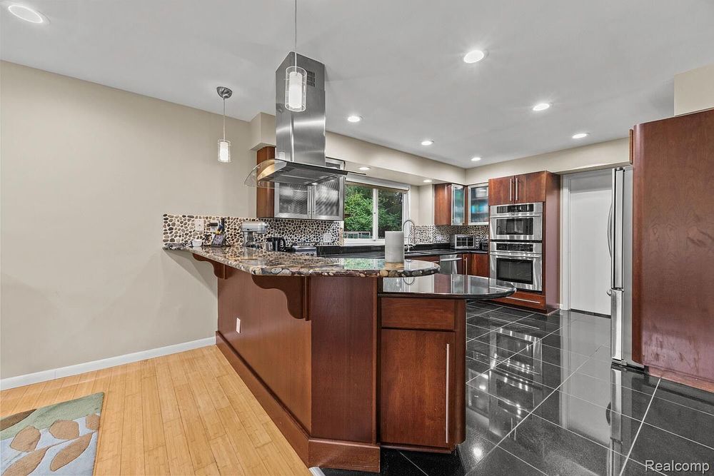 Spacious kitchen with granite island, cherry cabinets, pendant lights, and mixed tile and hardwood floors.