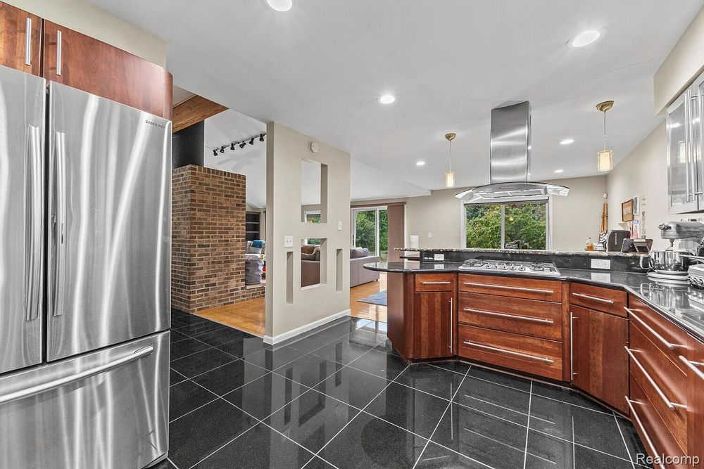 Open kitchen with stainless steel refrigerator, cherry wood cabinets, island cooktop, and black tile floors.